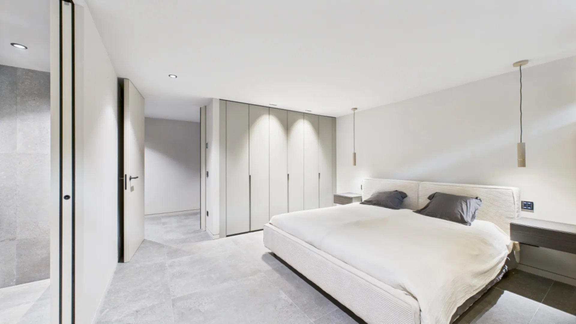 Modernes Schlafzimmer mit großem Bett, Einbauschränken und grauem Fliesenboden.