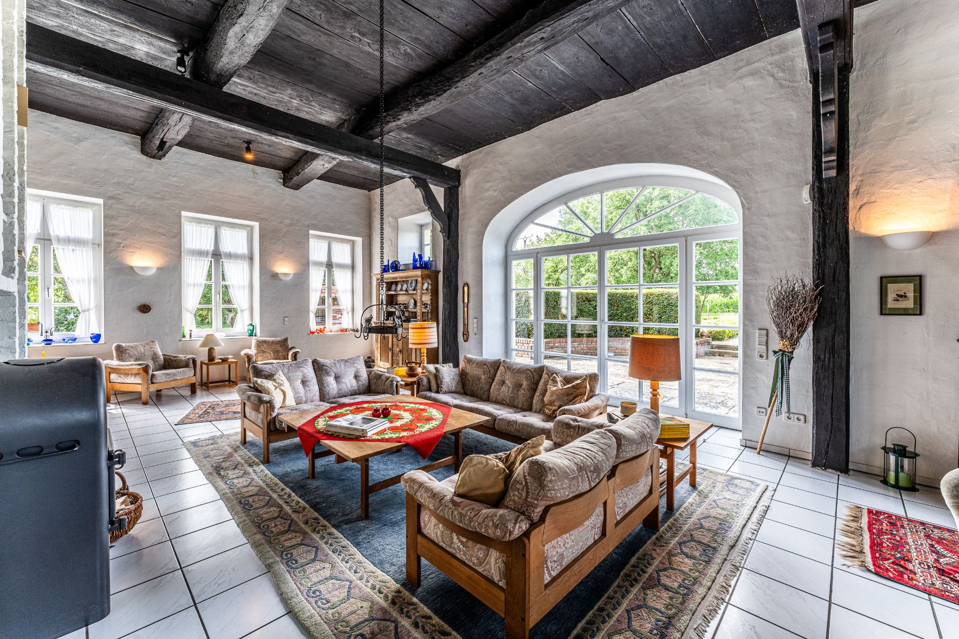 Helles Wohnzimmer mit großen Fenstern, Holzbalken, Sofas und Teppichen.