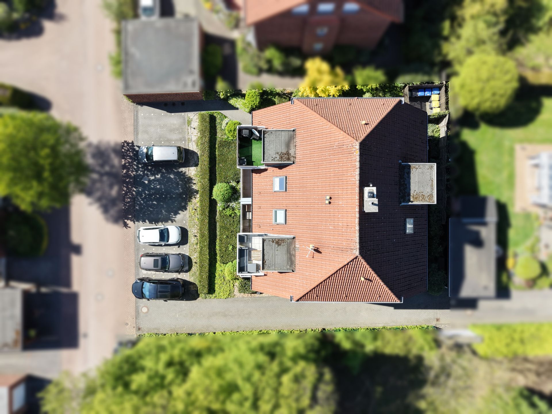 Luftaufnahme eines Wohnhauses mit rotem Dach, Parkplatz und Garten.