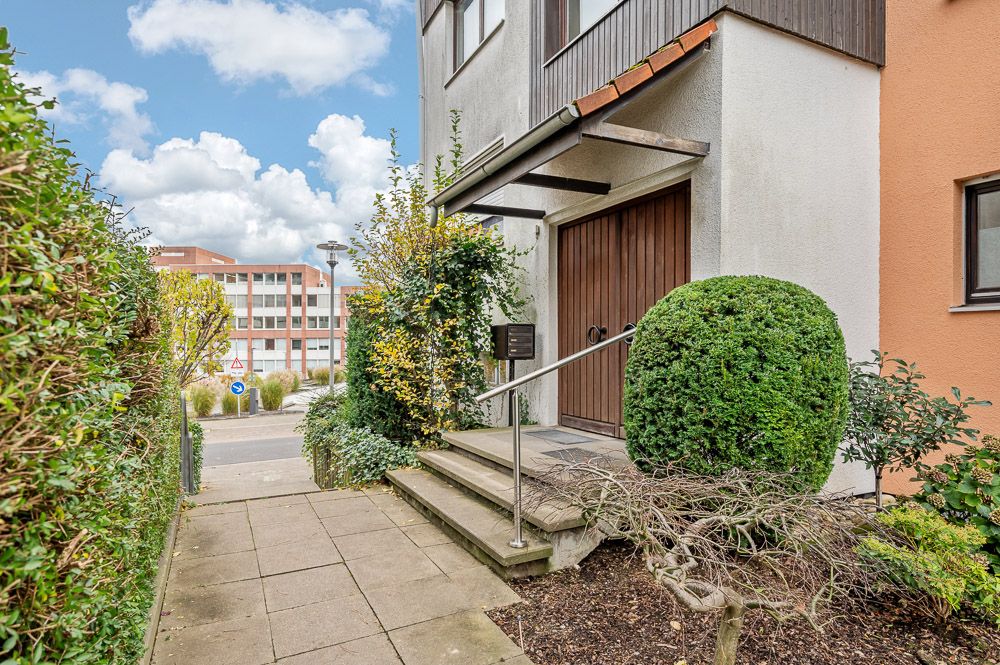 Eingang eines Wohnhauses mit Treppe, Geländer und gepflegten Büschen daneben.