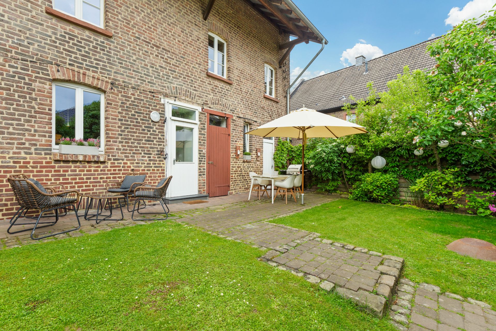 Garten mit Rasen, Gartenmöbeln und Sonnenschirm an einem Backsteinhaus.