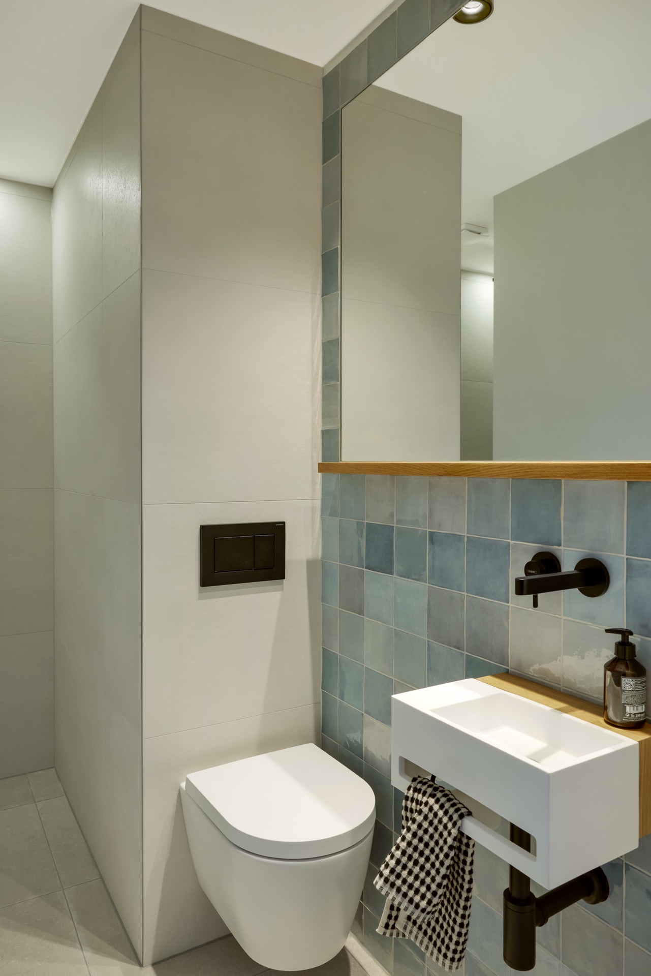 Modernes Badezimmer mit Wandtoilette, kleinem Waschbecken und blauen Fliesen.