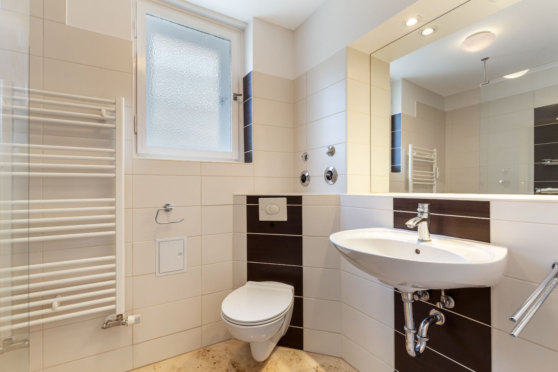 Modernes Bad mit Wandwaschbecken, Toilette, Handtuchheizkörper und Fenster.