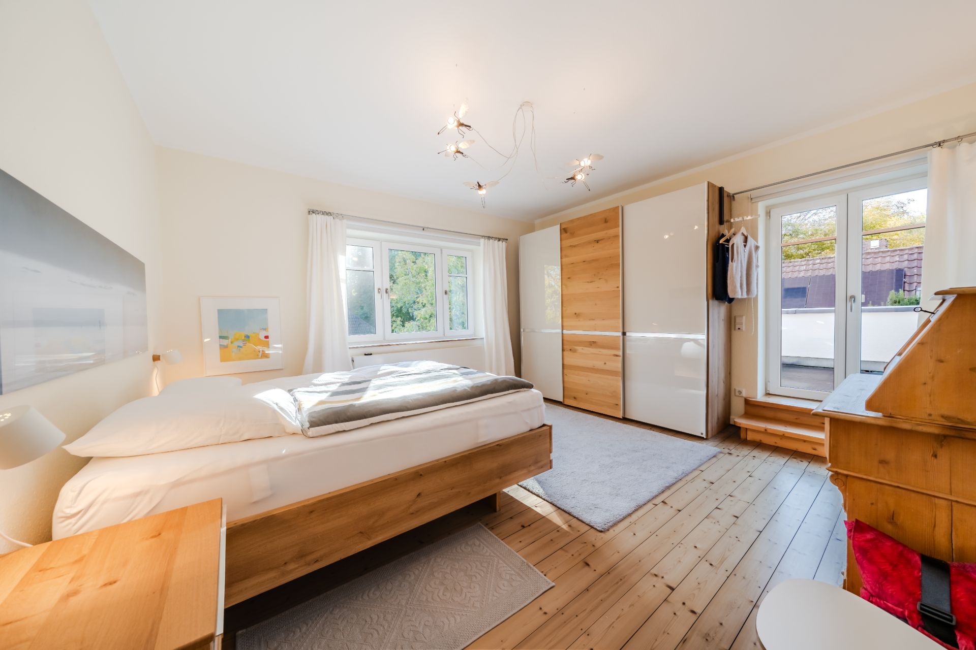Helles Schlafzimmer mit Holzboden, Doppelbett, Kleiderschrank und Zugang zu einem Balkon.