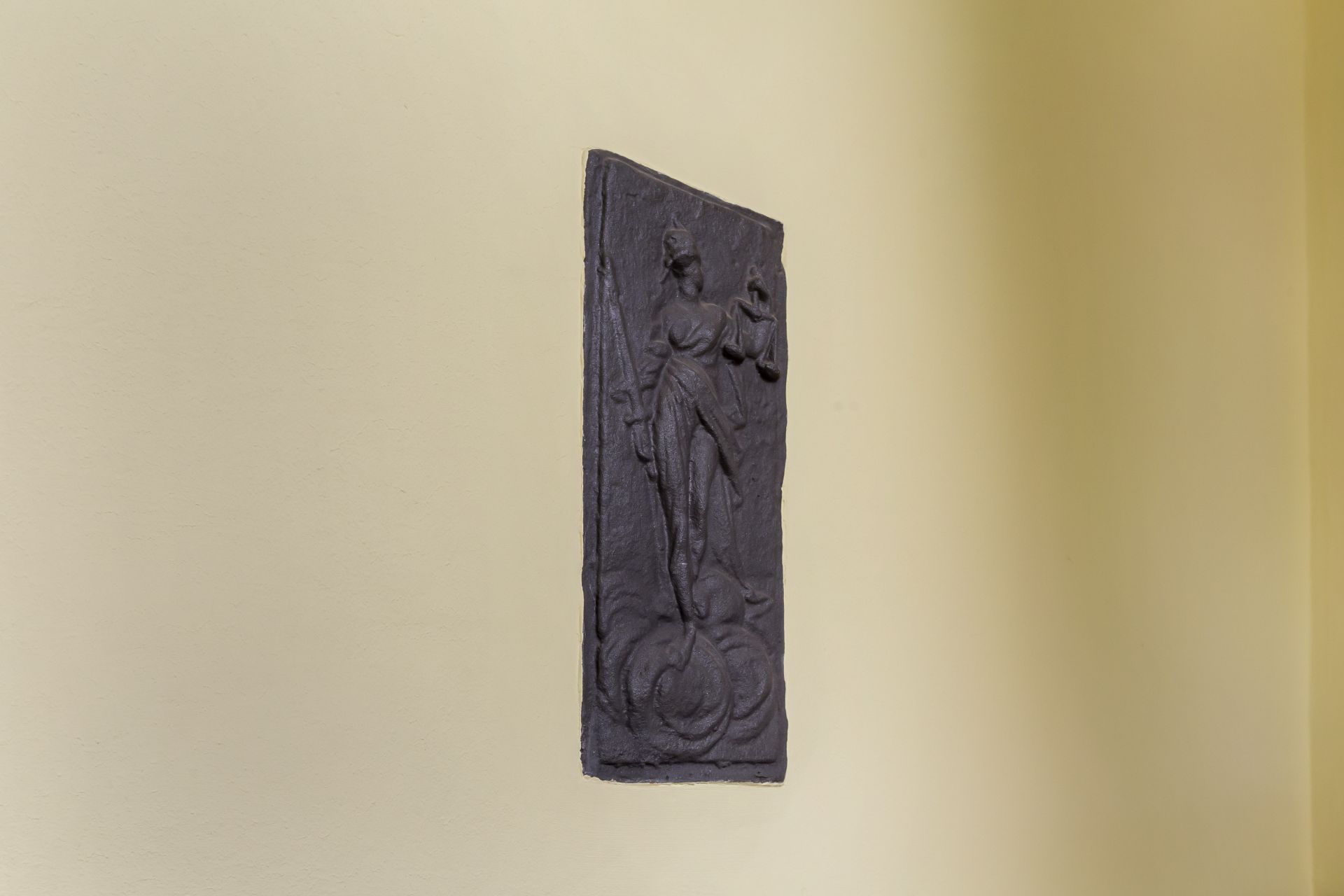 Dunkles Relief einer stehenden Figur an einer hellen Wand.
