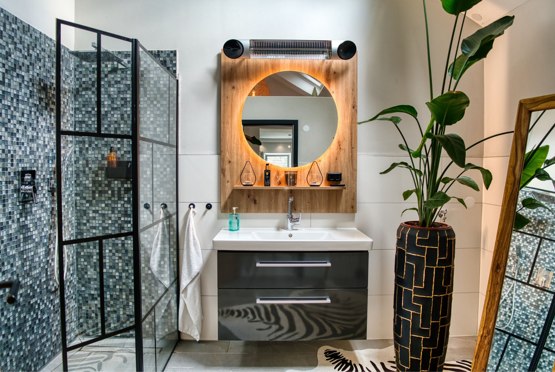 Modernes Badezimmer mit Glasdusche, Holzspiegel, Waschbecken und großer Pflanze im Designer-Topf.