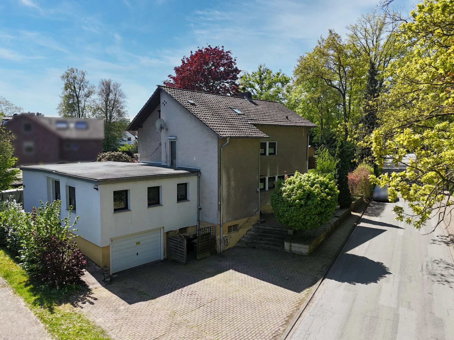 Wohnhaus mit Garage, umgeben von Bäumen und einer gepflasterten Einfahrt.