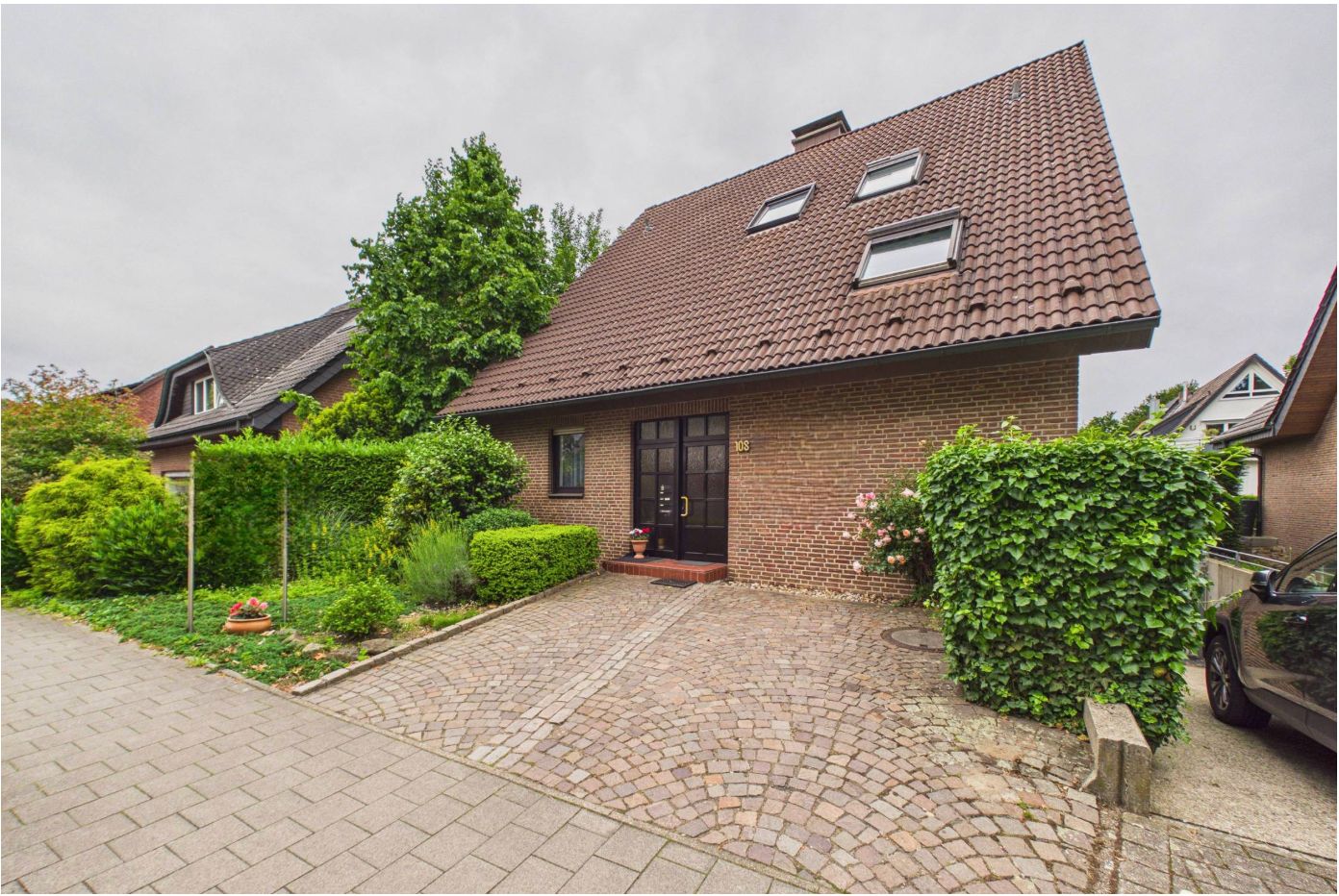 Einfamilienhaus mit rotem Ziegeldach, Vorgarten und gepflasterter Einfahrt.