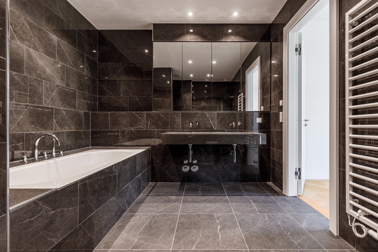 Modernes Badezimmer mit dunklen Fliesen, Badewanne, Doppelwaschbecken und großem Spiegel.