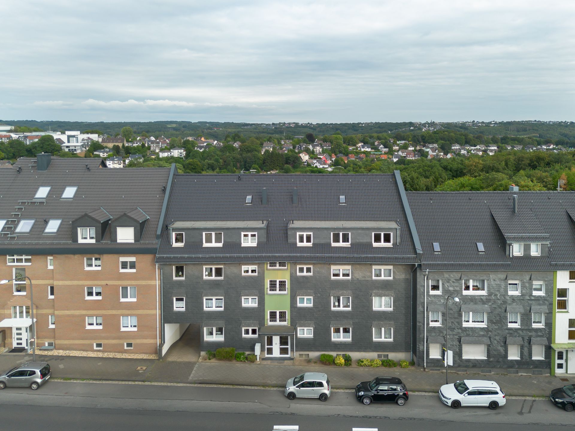 Mehrfamilienhaus mit grauer Fassade, mehrere Autos parken davor an der Straße.