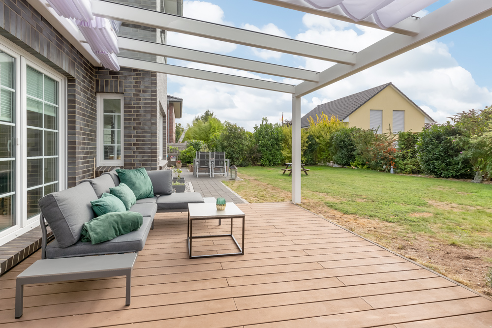 Überdachte Terrasse mit grauem Sofa, kleinem Tisch und Blick in den Garten.