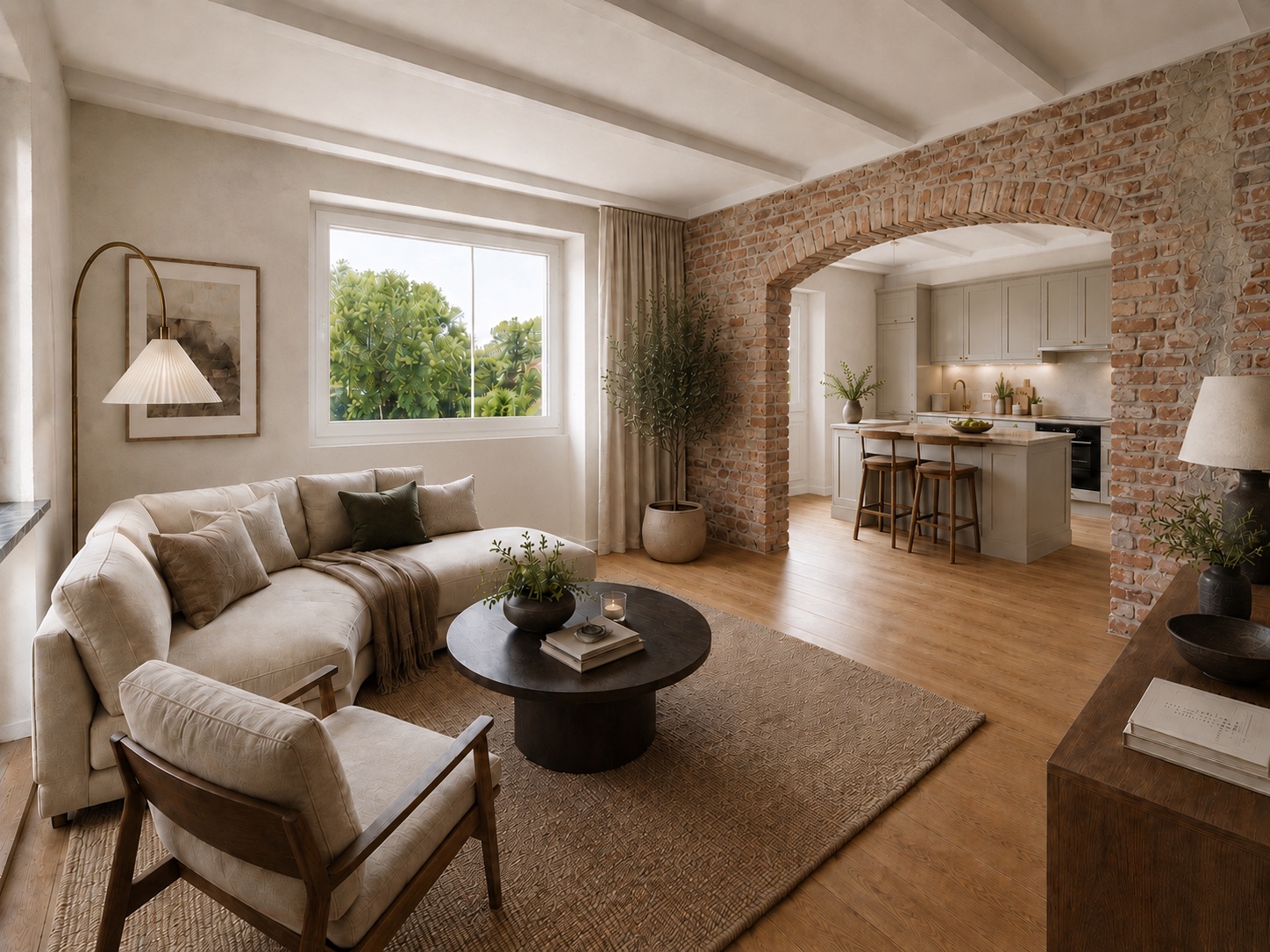 Helles Wohnzimmer mit Sofa, Sessel, rundem Tisch und offener Küche mit Backsteinbogen.