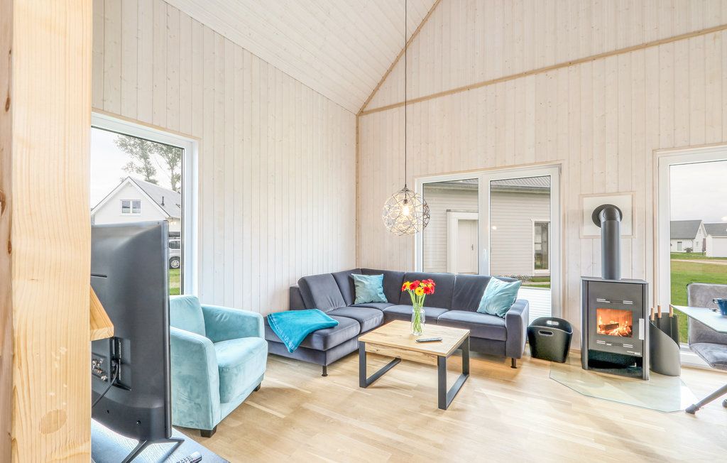 Helles Wohnzimmer mit Ecksofa, Sessel, Holztisch, Kaminofen und großen Fenstern.
