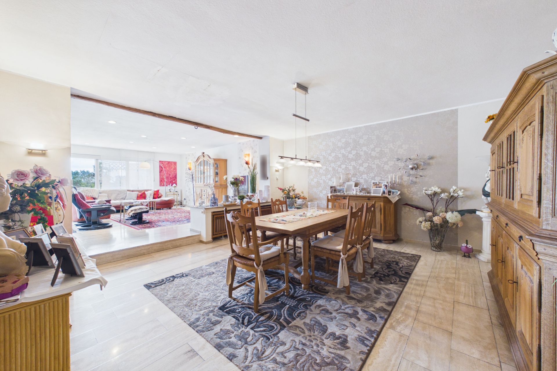Helles Esszimmer mit Holzmöbeln, Teppich und Blick in ein Wohnzimmer mit großen Fenstern.