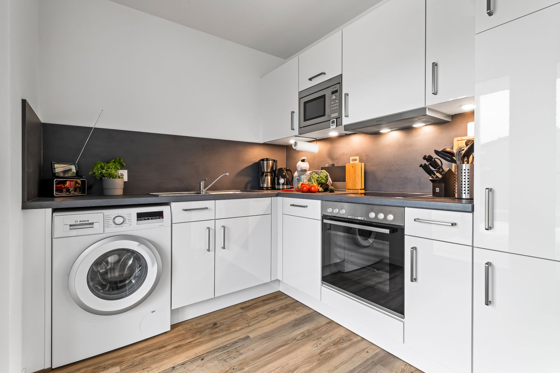 Moderne Einbauküche mit Waschmaschine, Backofen, Mikrowelle und weißen Schränken.