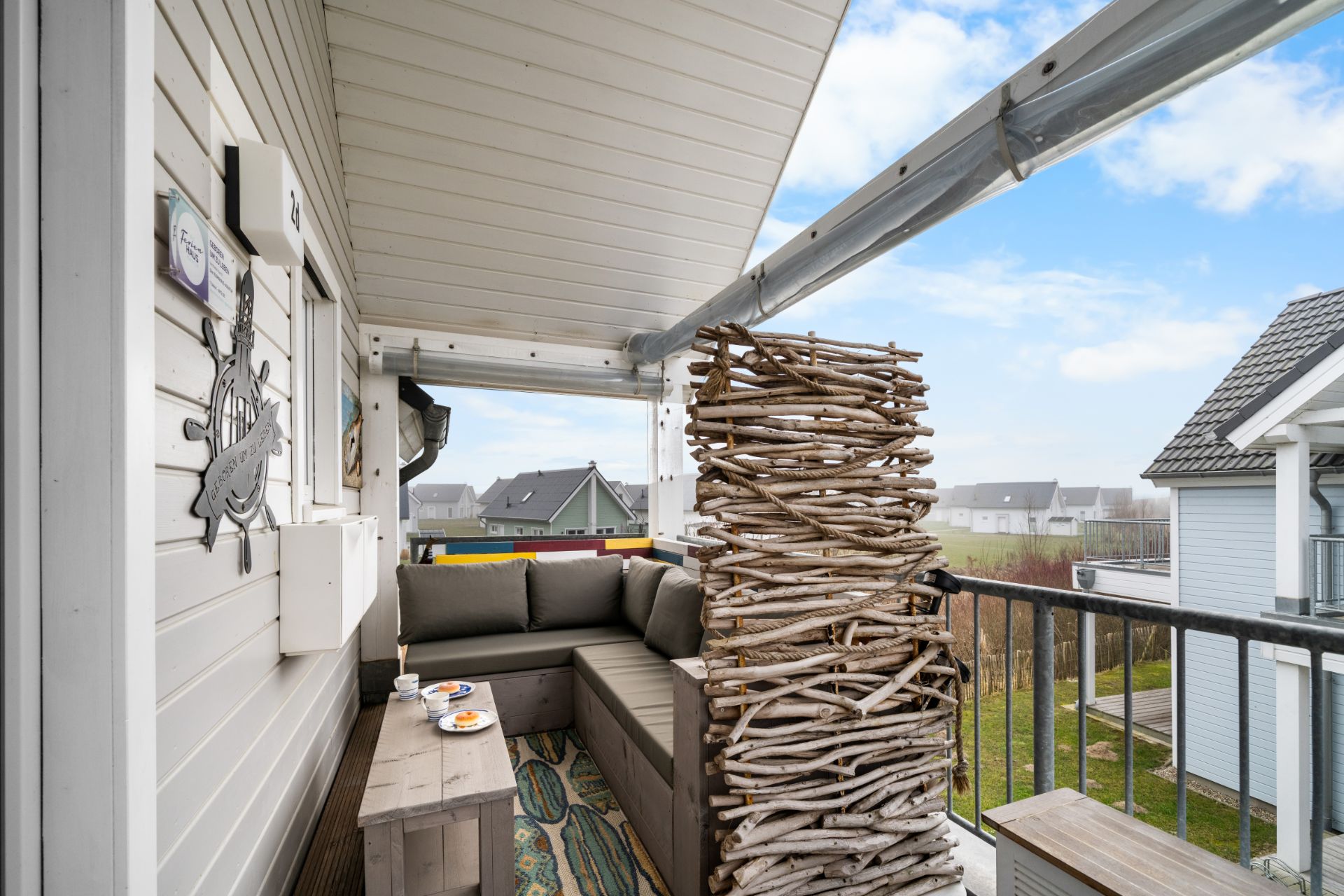 Überdachter Balkon mit Sitzbank, kleinem Tisch und Holzdeko, Blick auf Nachbarhäuser.