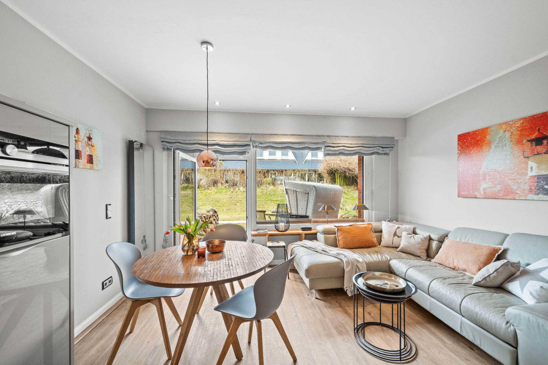 Helles Wohnzimmer mit großem Fenster, Esstisch, grauem Sofa und moderner Dekoration.