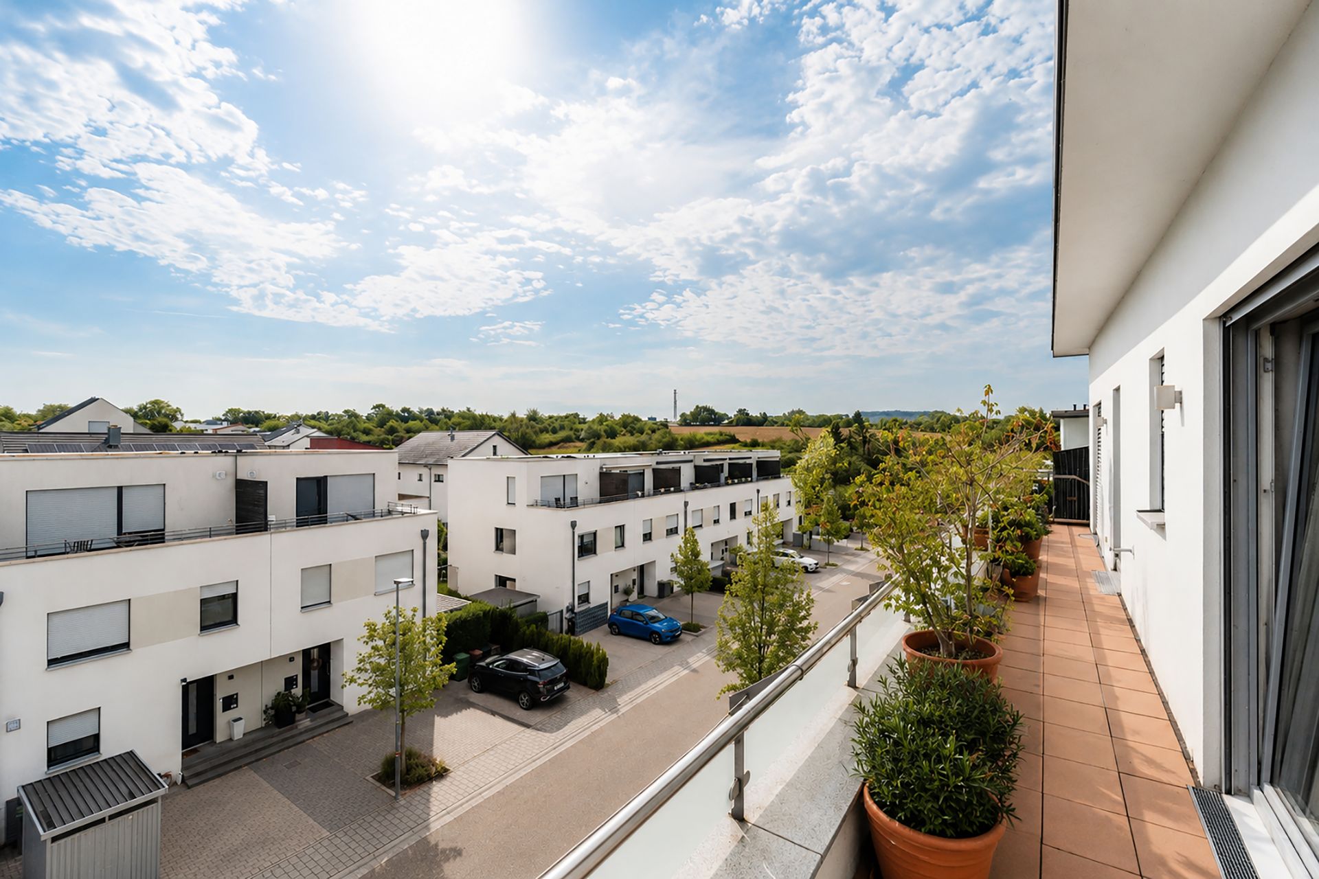 Blick von einem Balkon auf eine ruhige Wohnstraße mit modernen weißen Häusern und Bäumen.