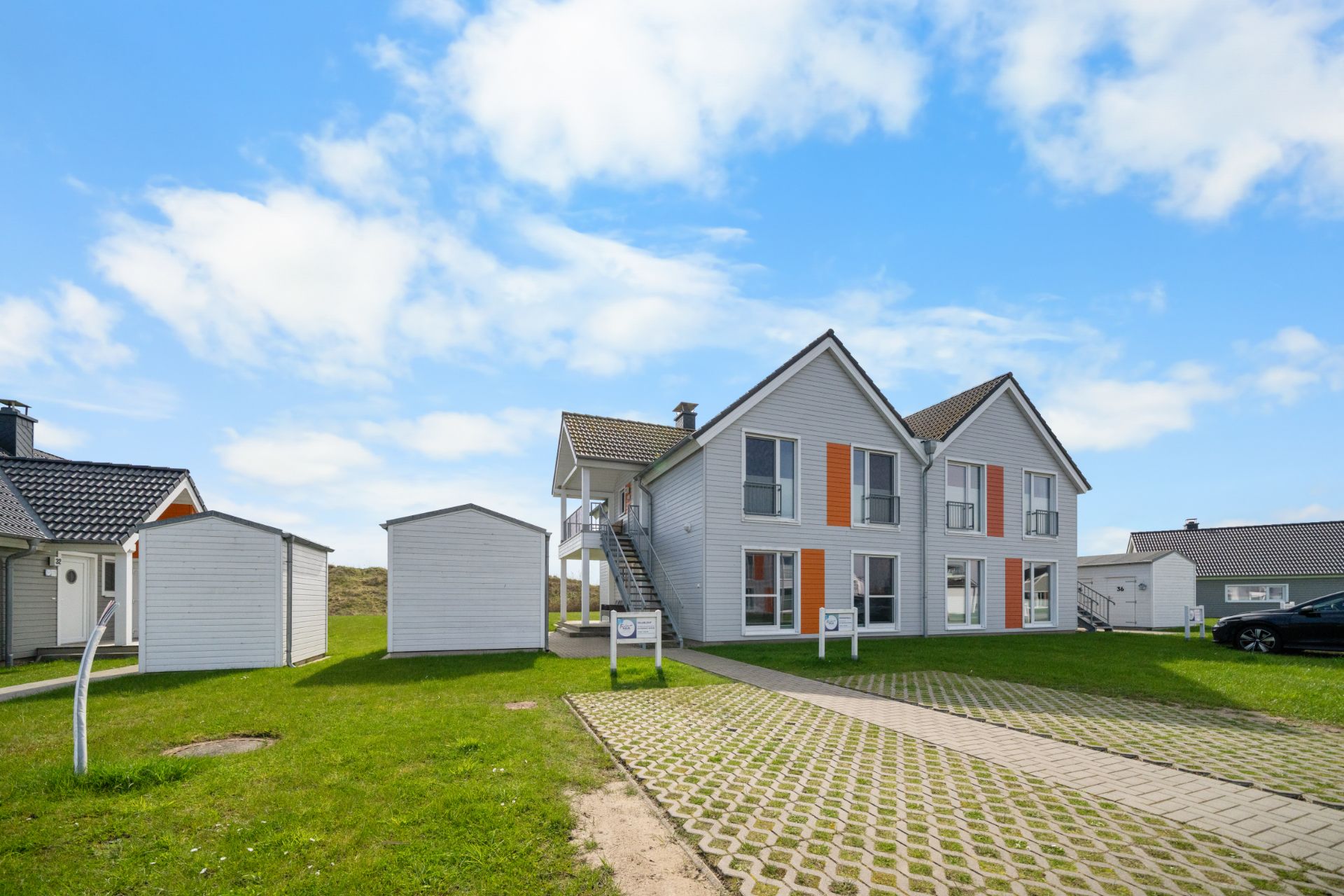 Modernes zweistöckiges Wohnhaus mit weißen Fassaden und orangen Akzenten, grüner Rasen und Nebengebäude.