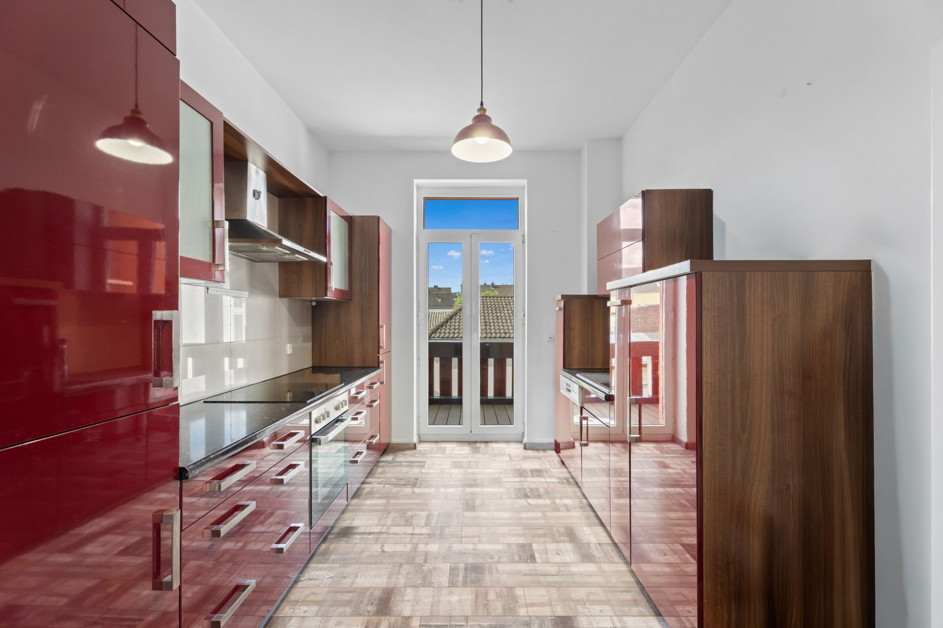 Moderne Küche mit roten Hochglanzschränken und Fenster mit Blick auf Balkon.