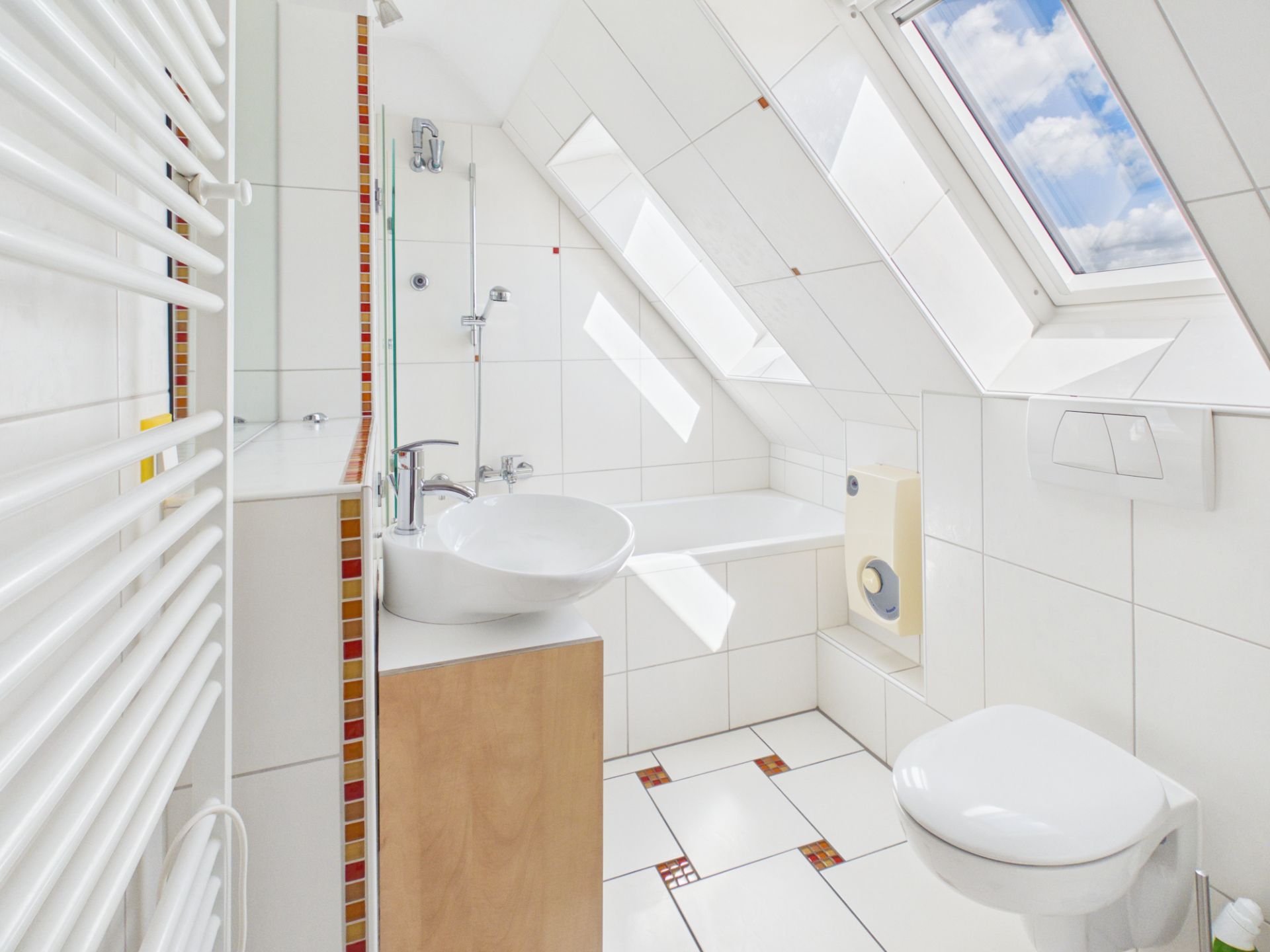 Helles Badezimmer mit Dachschräge, Badewanne, Waschbecken, WC und Dachfenster.