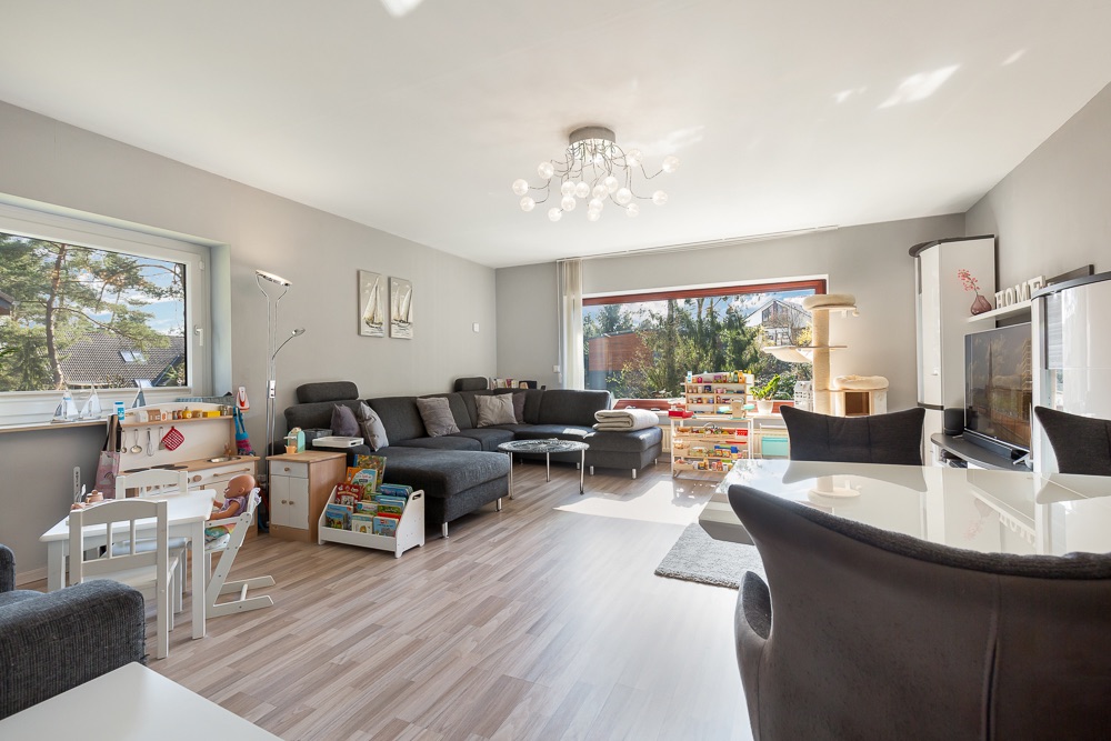 Helles Wohnzimmer mit Spielsachen, großem Sofa, Esstisch und großen Fenstern mit Ausblick.
