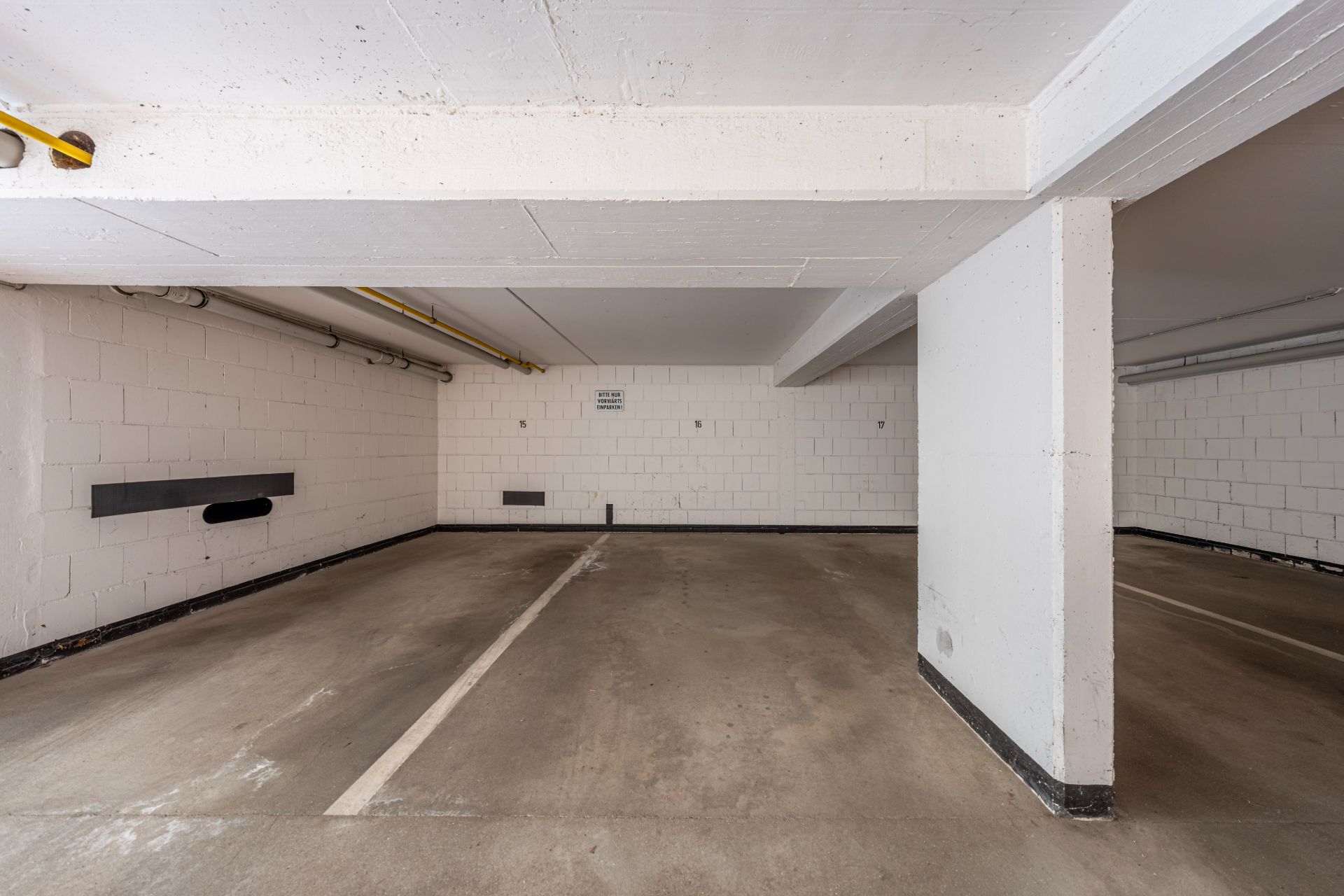 Leerer Tiefgaragenstellplatz mit weiß gestrichenen Wänden und Markierungen auf dem Boden.