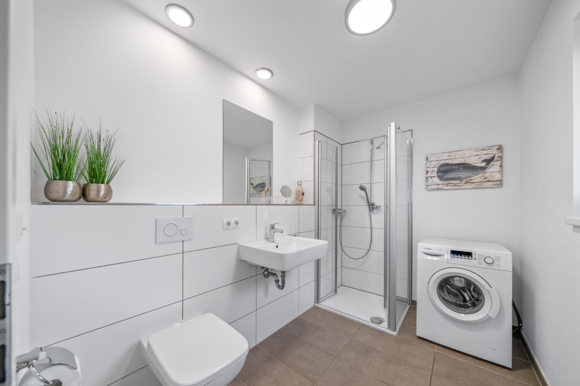 Modernes Badezimmer mit Dusche, Waschbecken, Toilette, Waschmaschine und dekorativen Pflanzen.