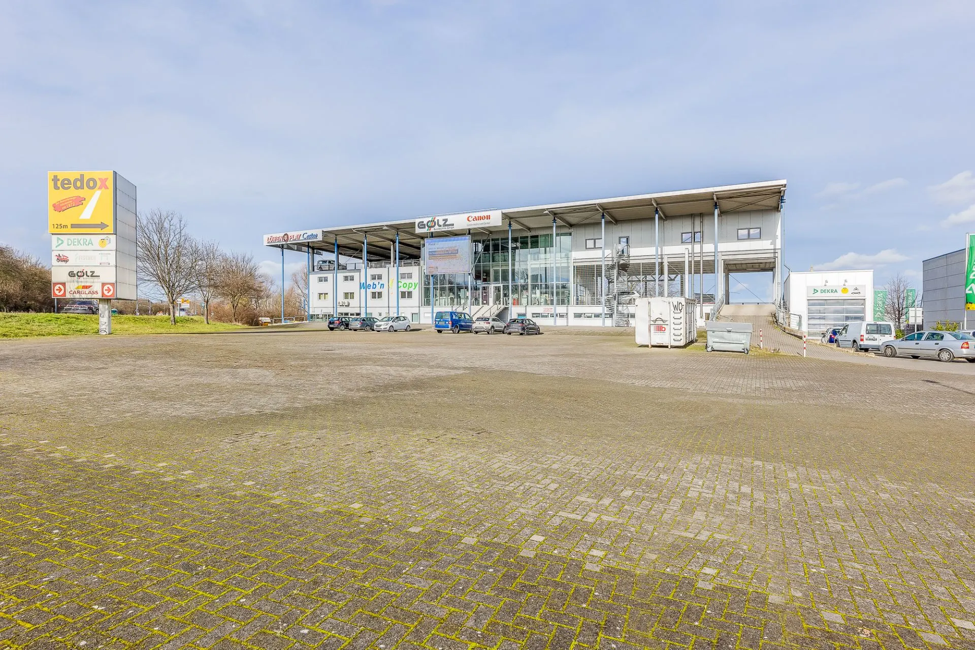 Großer Parkplatz vor einem modernen Geschäftsgebäude mit mehreren geparkten Autos.