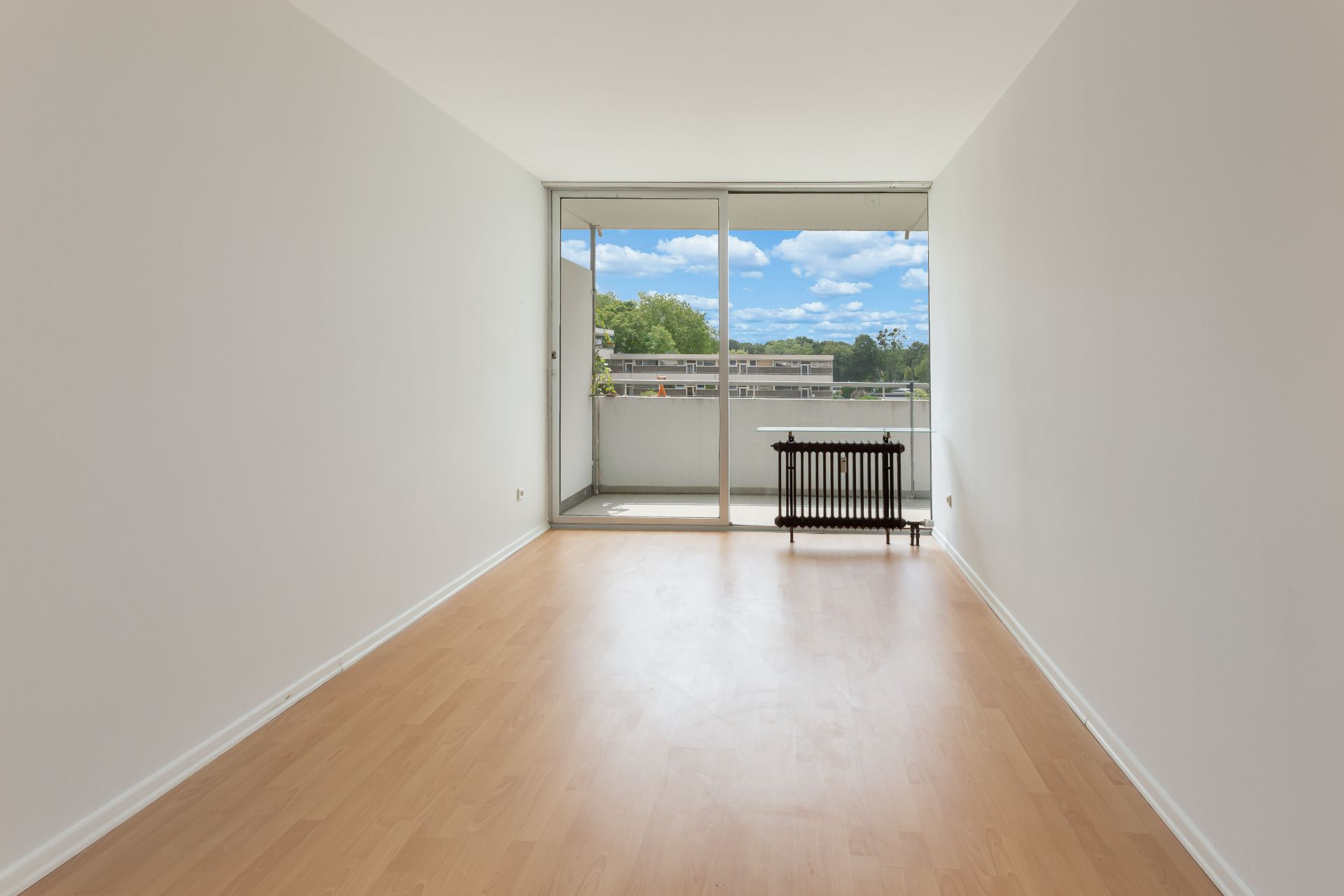 Leerer Raum mit Holzfußboden, großer Fensterfront und Zugang zu einem Balkon.