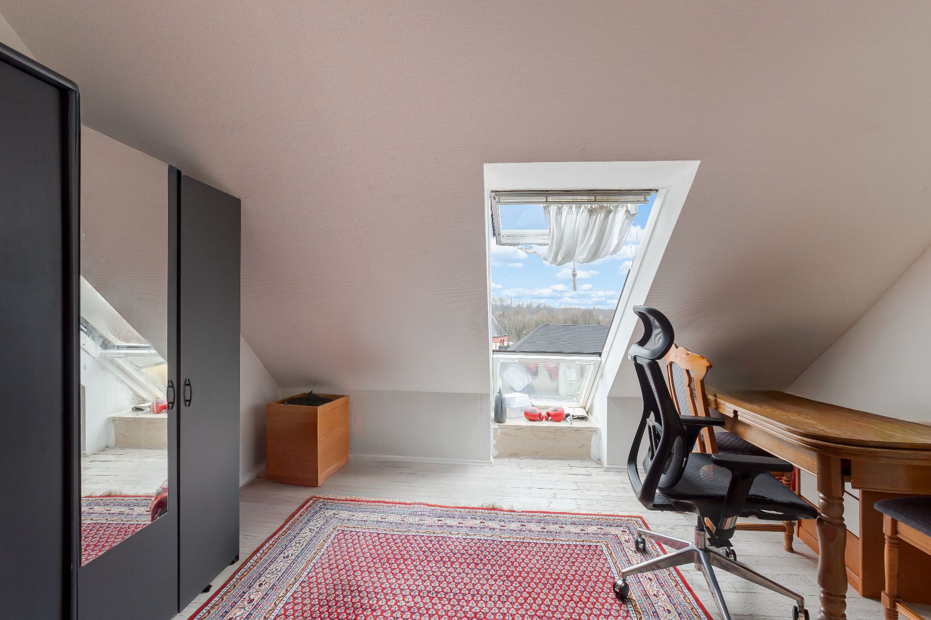 Dachzimmer mit Schreibtisch, Stuhl, Kleiderschrank, Fenster und Teppich.