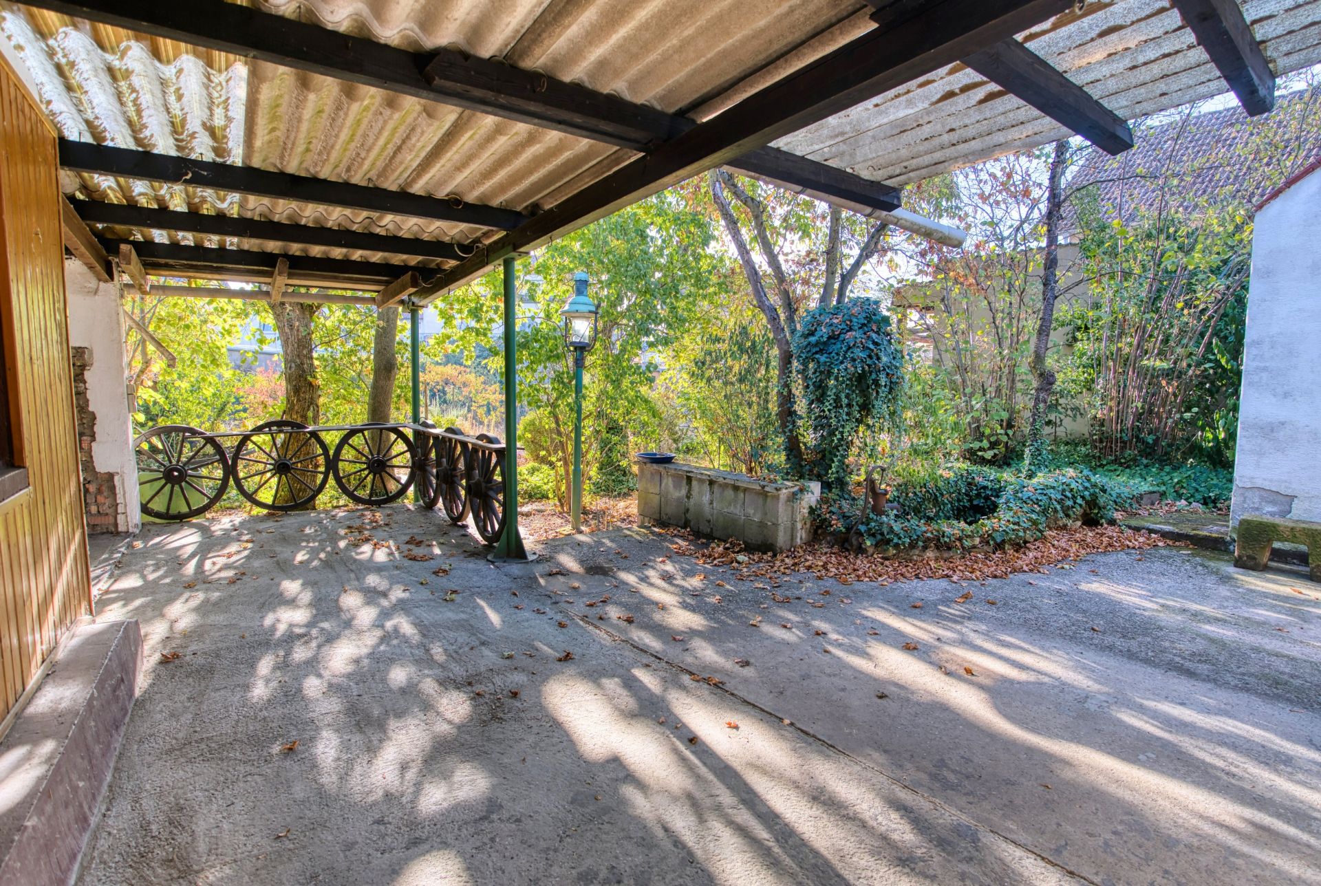 Überdachte Terrasse mit Wagenrad-Geländer, Blick auf Bäume und einen Garten.