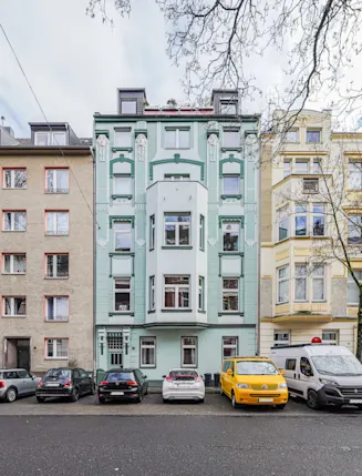 Mehrstöckige Wohnhäuser mit Autos auf der Straße davor, Bäume ohne Blätter am Rand.