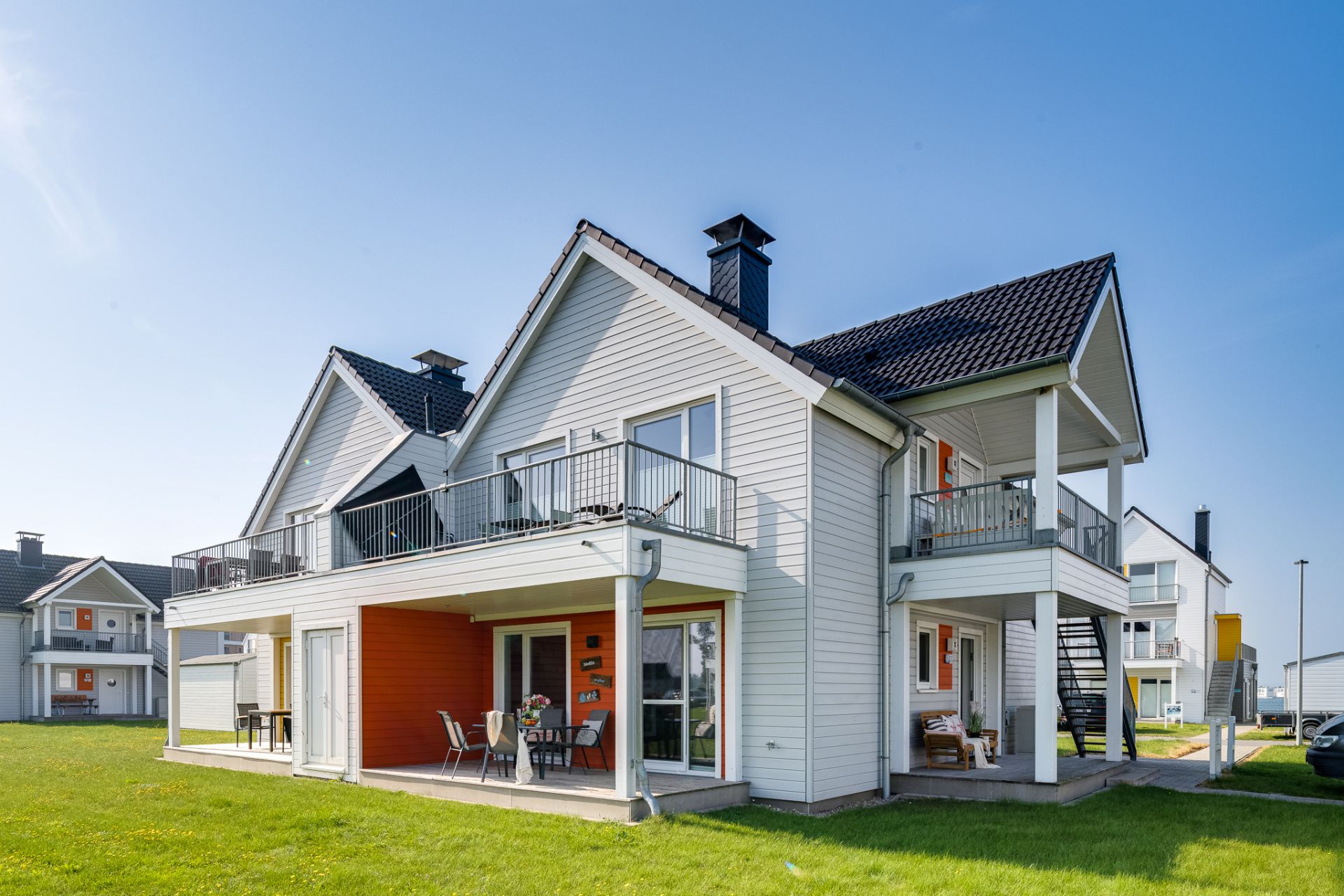 Modernes zweistöckiges Wohnhaus mit Balkonen, Terrasse und Rasenfläche.