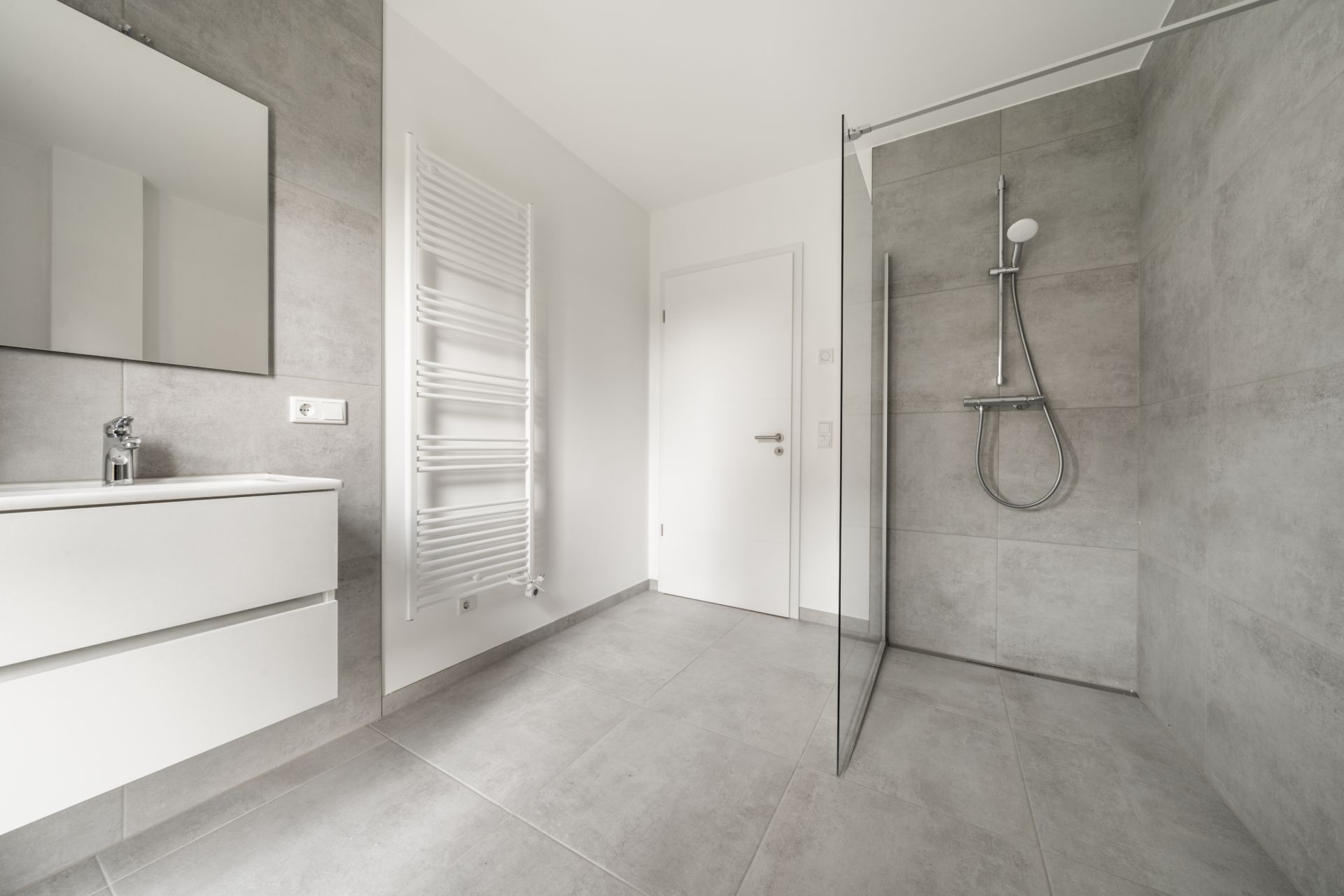 Modernes, helles Badezimmer mit ebenerdiger Dusche, Waschbecken und Handtuchheizkörper.