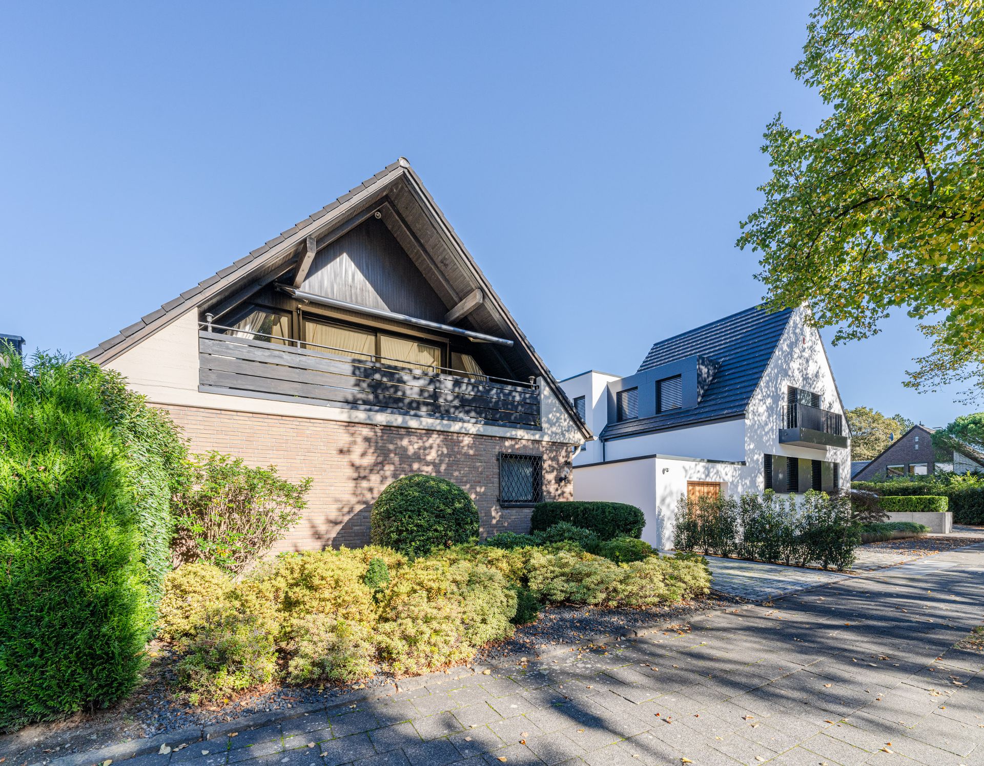 Zwei moderne Einfamilienhäuser mit Gärten und gepflastertem Weg bei sonnigem Wetter.