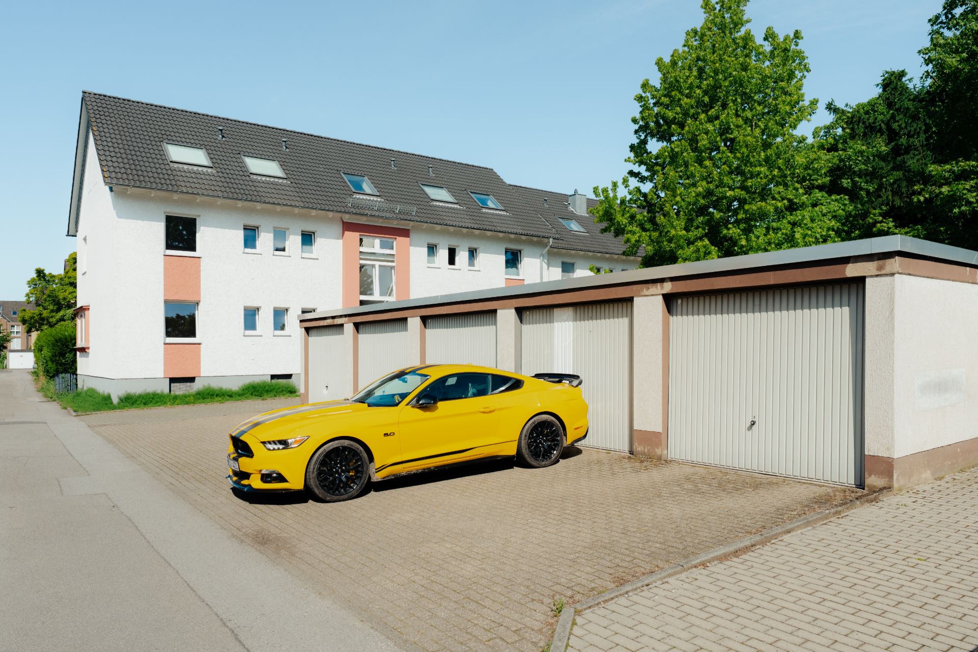 Gelbes Auto steht vor Garagen neben einem weißen Wohngebäude mit mehreren Fenstern.