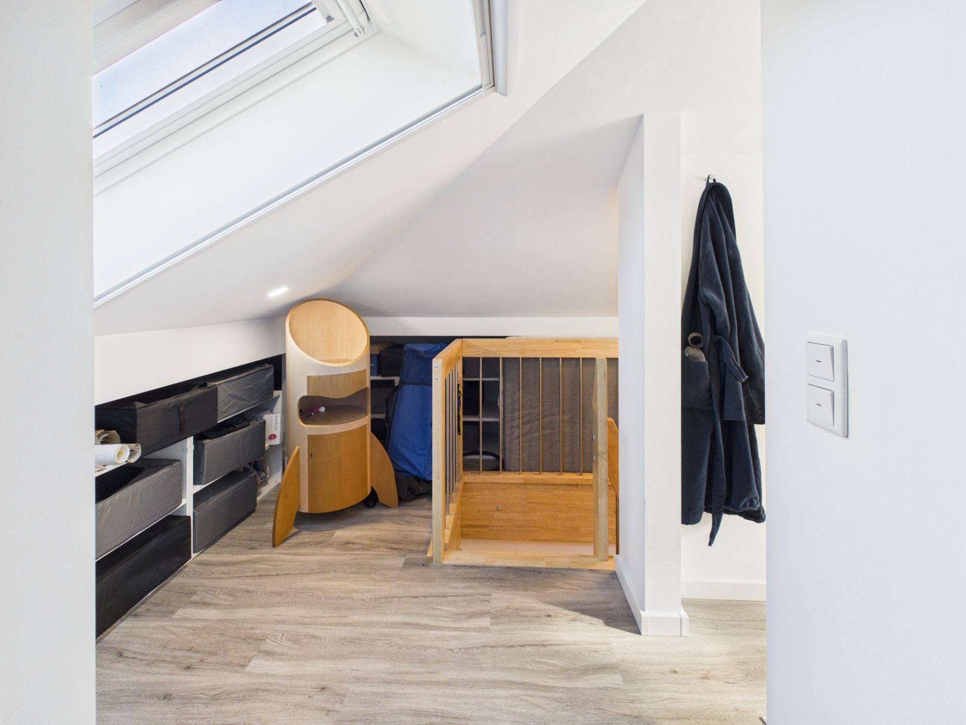 Dachzimmer mit Holzspielzeug, Schubladen und Dachfenster, ein Mantel hängt an der Wand.
