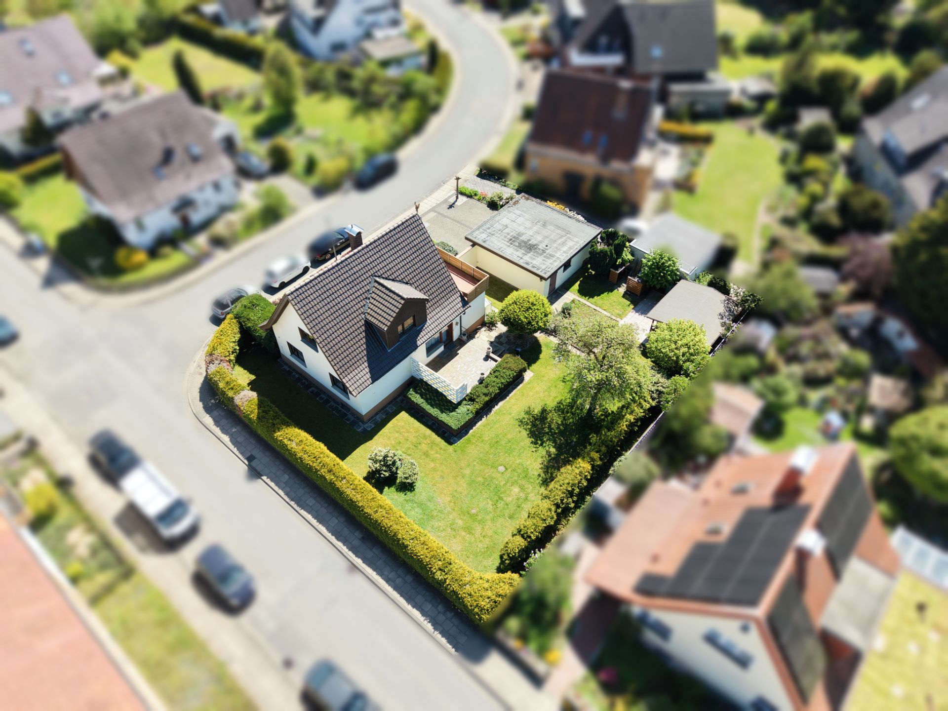 Luftaufnahme eines Einfamilienhauses mit Garten und Nebengebäude an einer Ecke in einer Wohnsiedlung.