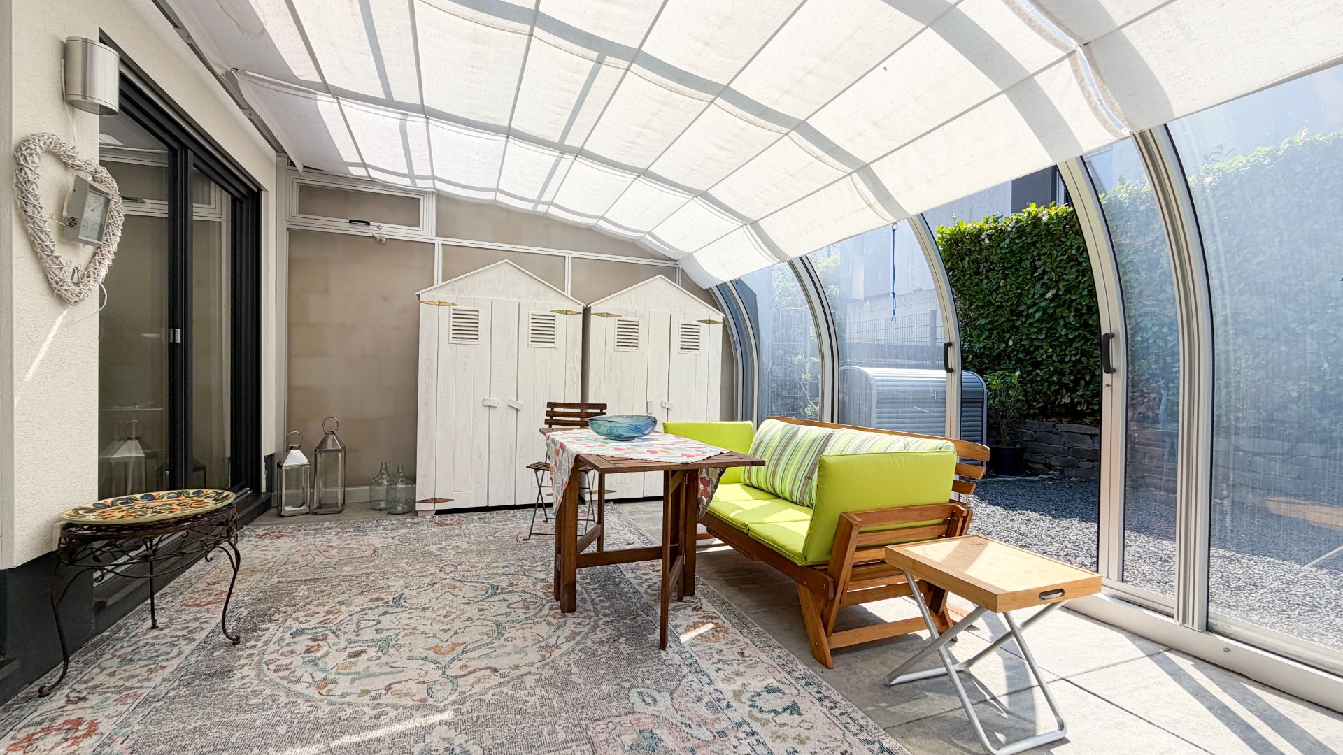 Überdachte Terrasse mit Sitzbank, Tisch, Stühlen und weißen Schränken, viel Tageslicht.