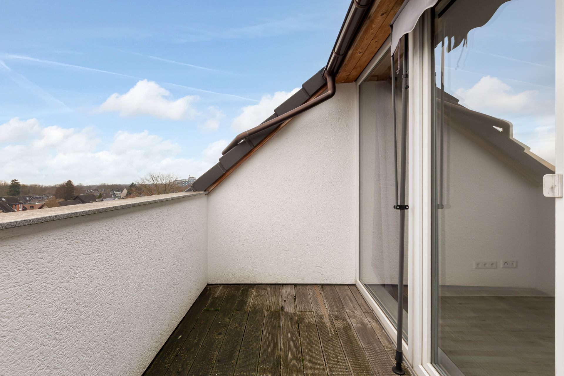 Kleine Dachterrasse mit Holzboden und Zugang durch eine große Glastür.