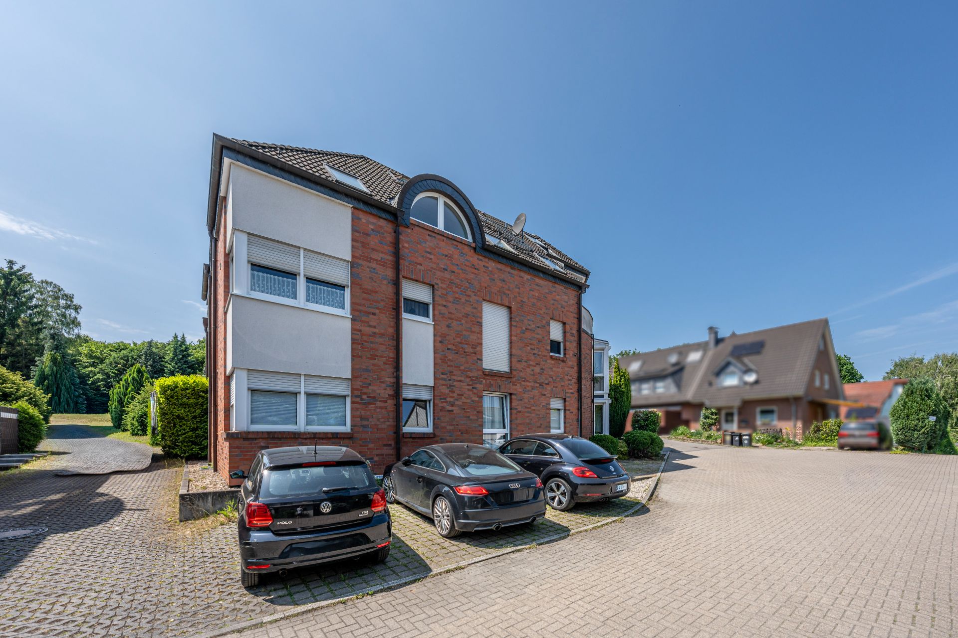 Mehrfamilienhaus mit gemischter Backstein- und Putzfassade, davor parken mehrere Autos.