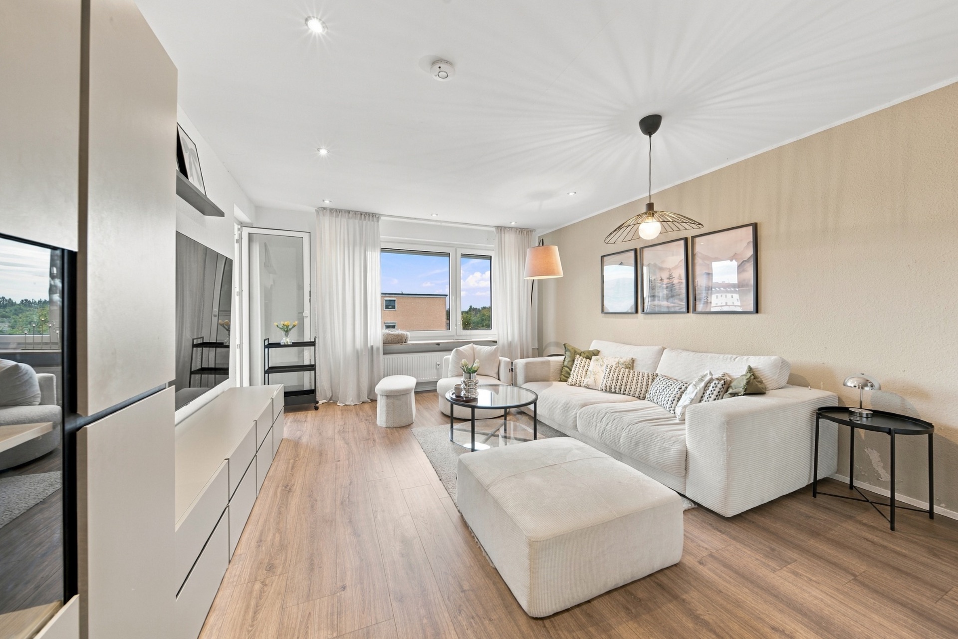 Modernes Wohnzimmer mit weißem Sofa, Holzboden, Couchtisch und großem Fenster mit Vorhängen.