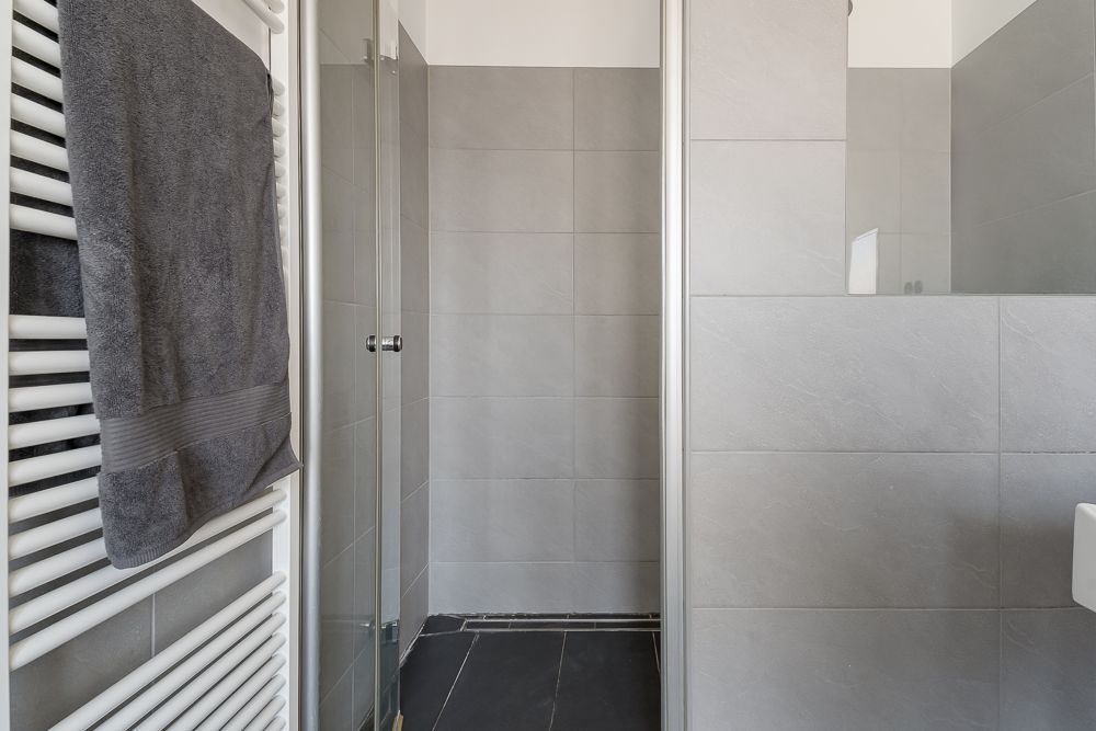 Modernes Badezimmer mit grauen Fliesen, Handtuchheizkörper und begehbarer Dusche.