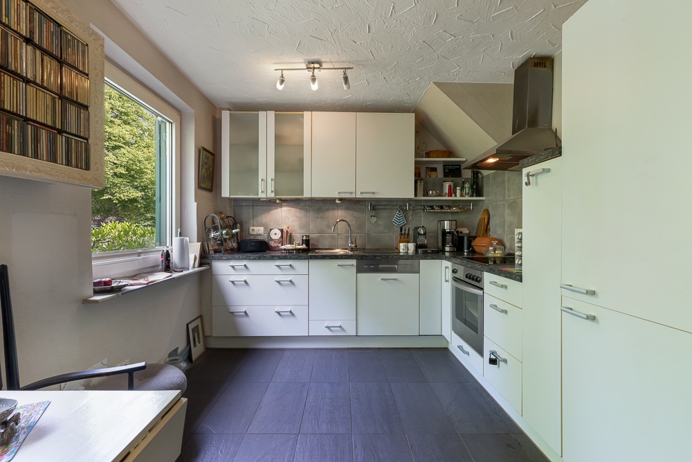 Moderne Einbauküche mit weißen Schränken, großem Fenster und Elektrogeräten.