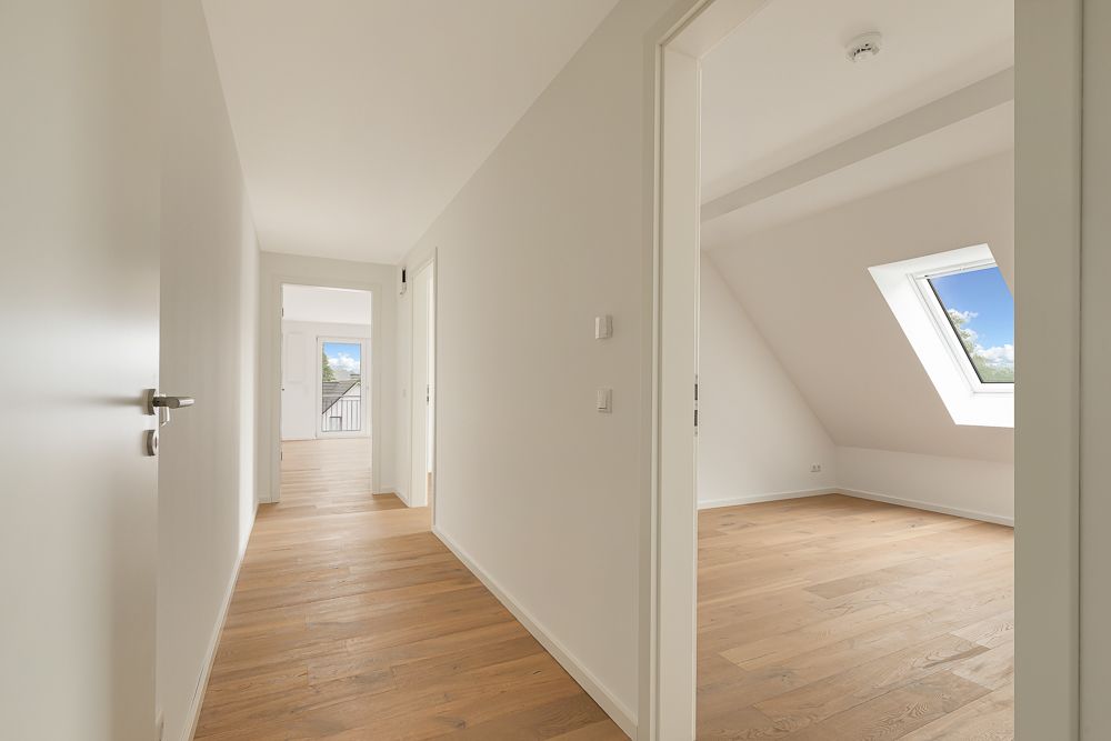 Heller Flur mit Holzboden, offene Türen zu Zimmern und Fenster mit Blick nach draußen.