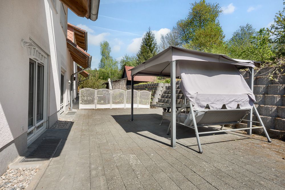 Große Terrasse mit Steinboden, Schaukelbank unter Pavillon und Sichtschutzzaun.