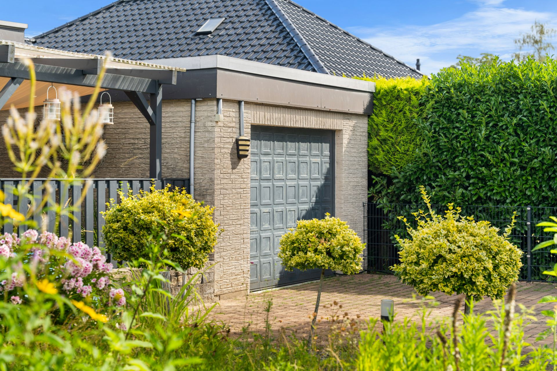 Garage aus Stein mit geschlossenem Tor, umgeben von Sträuchern und Bäumen im Garten.