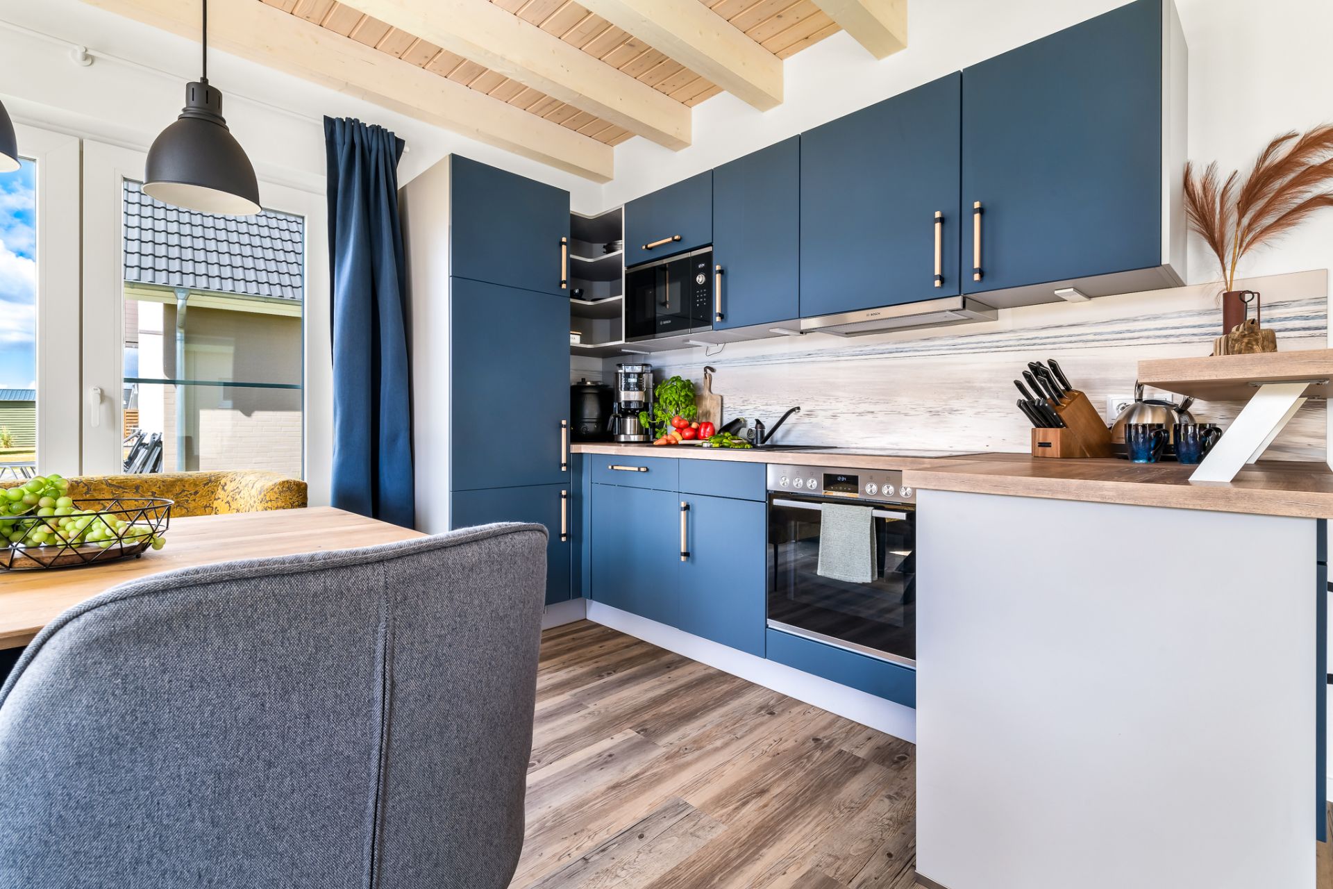Moderne Küche mit blauen Schränken, Holzboden und Esstisch mit Stuhl.