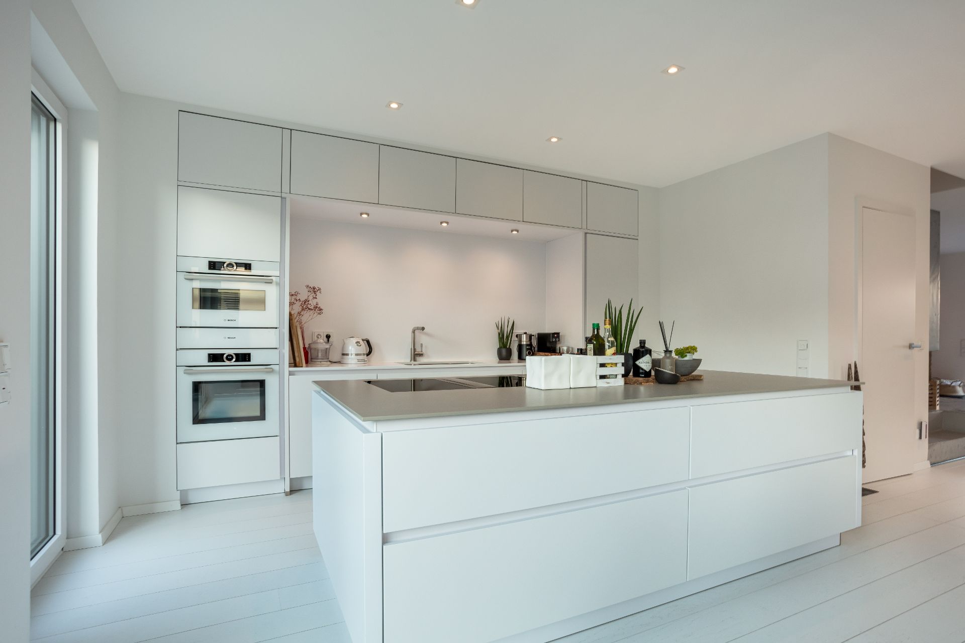 Moderne, helle Küche mit Kochinsel, Einbaugeräten und weißen Schränken.